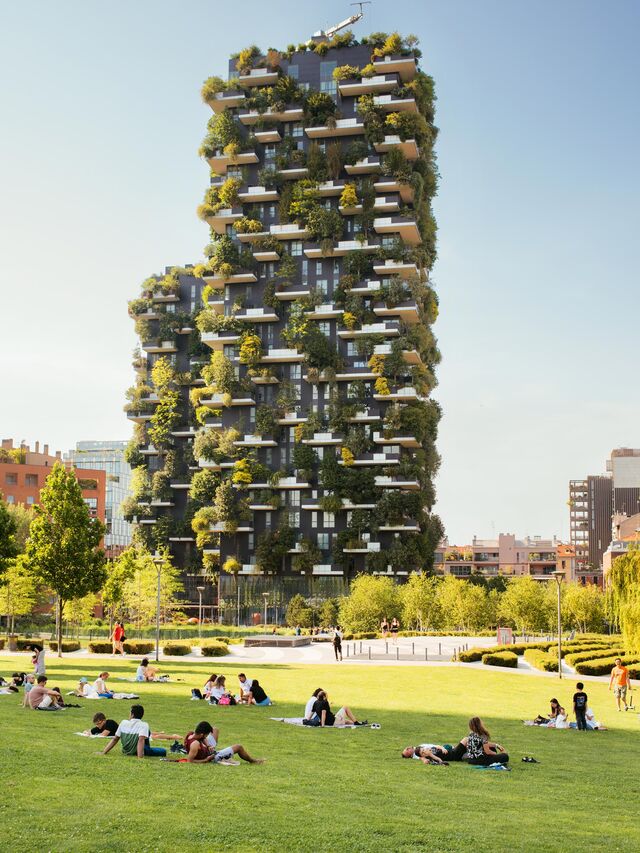 People sit on the tree-lined lawns in front of the plant-filled terraces of the Biblioteca degli Alberi Milano. 