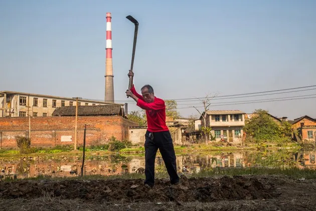 A farmer prepares his land to plant sweet potatoes beside a lead factory at Chenjiawan in the Hunan Province of China on Dec. 3, 2013