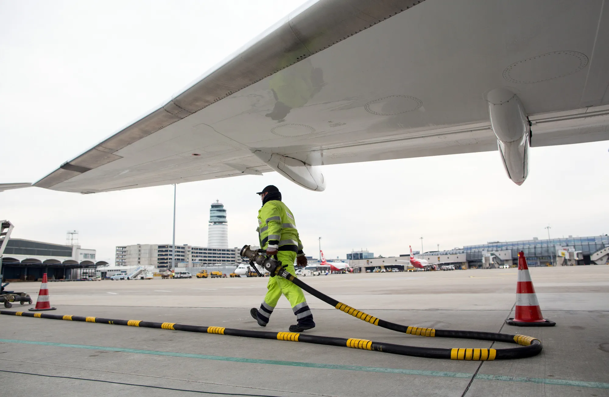 A ground crew worker carries a fuel pipe under a passenger aircraft on the tarmac.