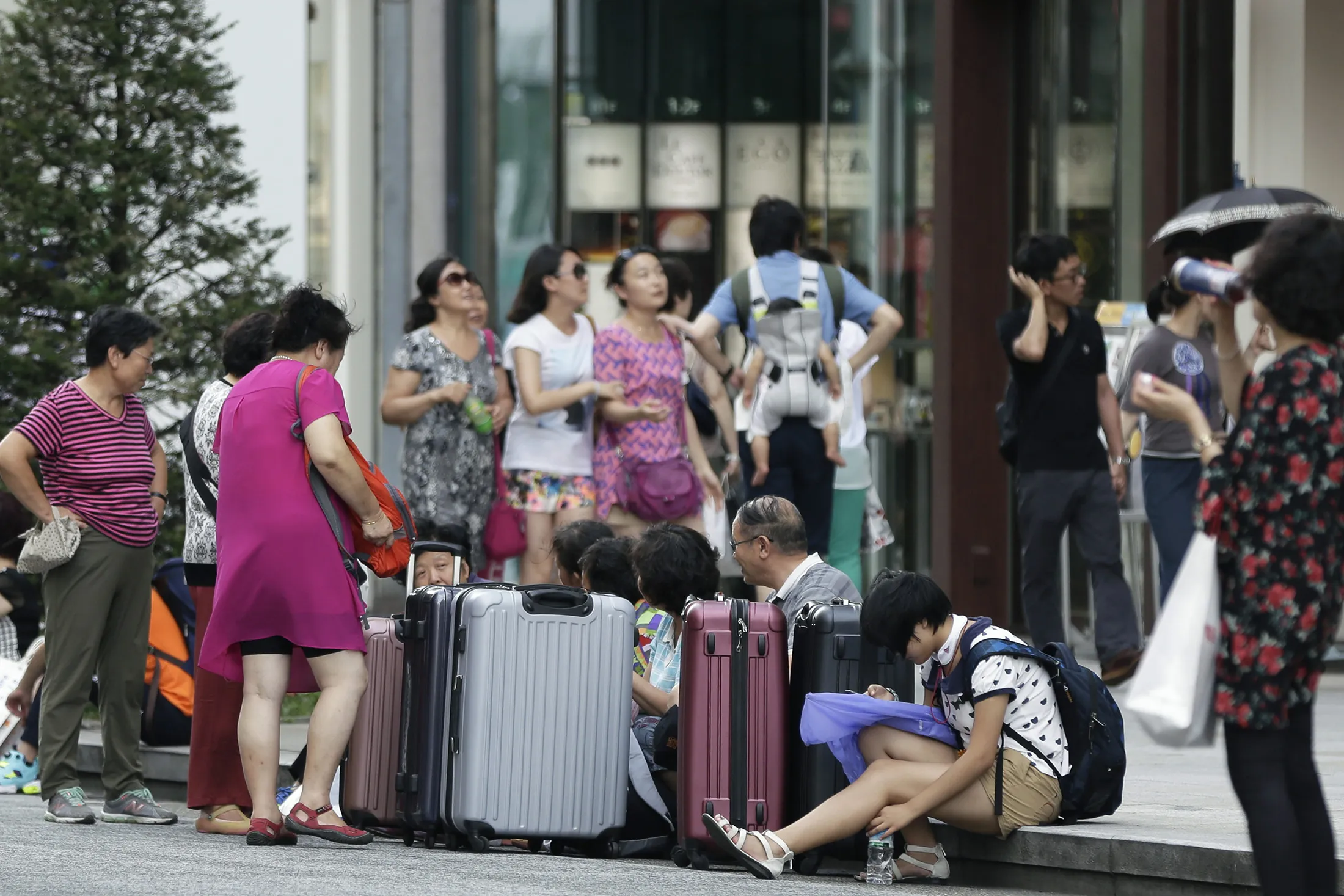 A group of Chinese tourists sit with their suitcases in the Ginza district of Tokyo, Japan.
