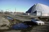 A car rounds the corner; instead of factories, now a domed structure (like a giant igloo) sits behind a long wire fence with concertina wire
