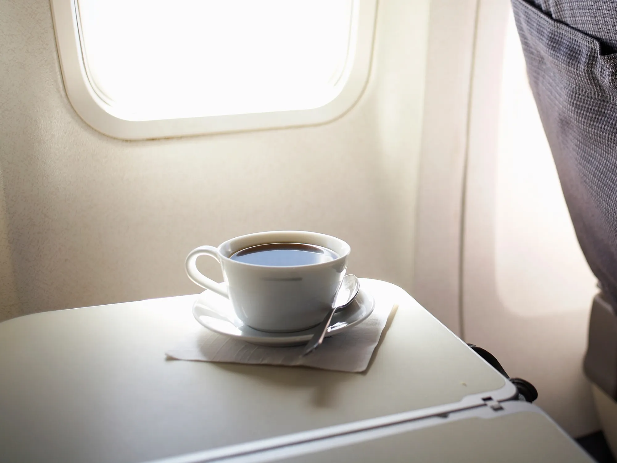Cup of coffee on airplane tray table by window, elevated view