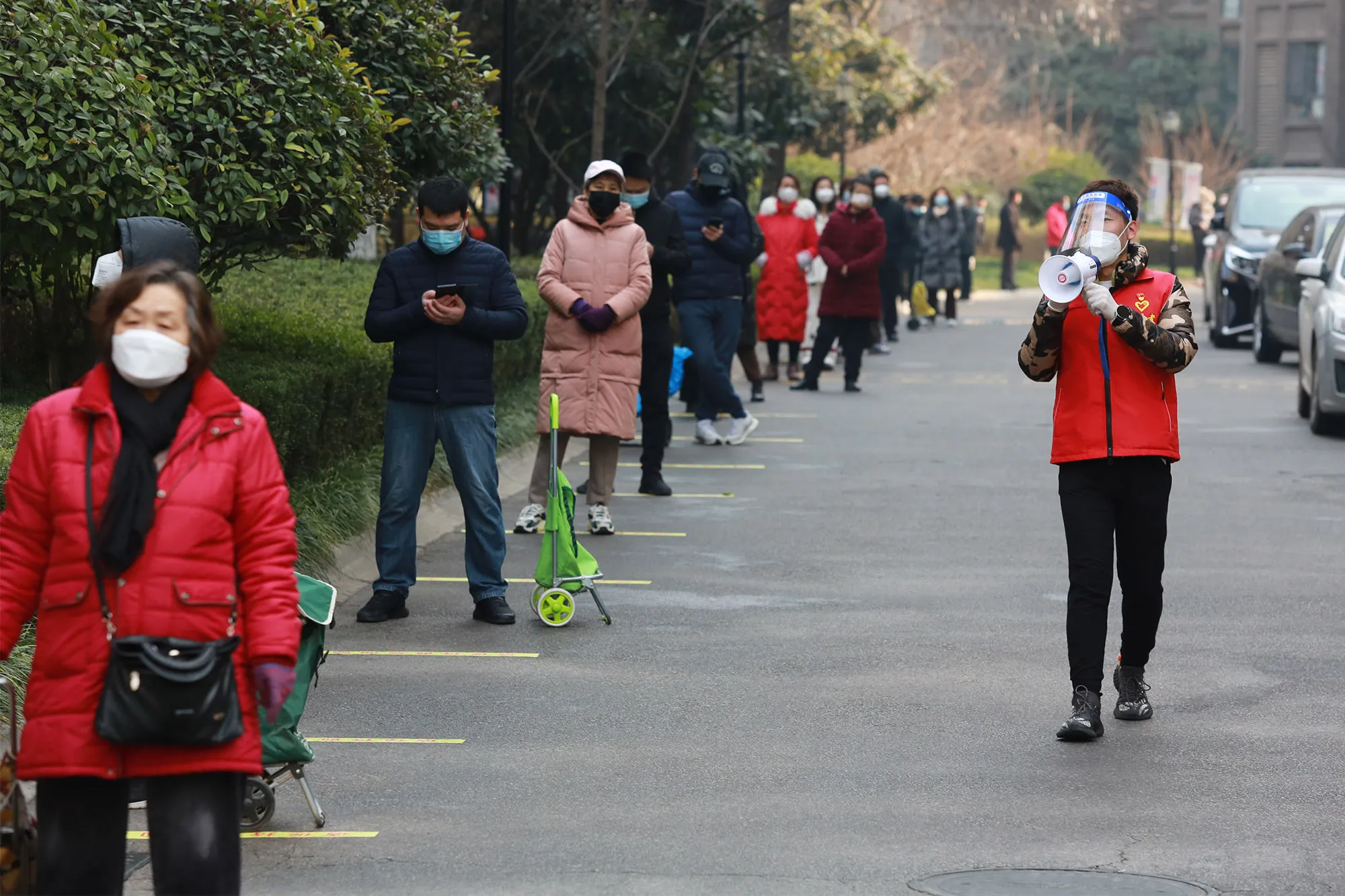 A volunteer reminds people of social distance as they line up to buy necessities near their residential block in Xian city in Shaanxi province, on Jan. 3.&nbsp;