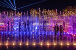 People stand inside a Christmas light show and synchronized fountain display at the Experience Park, in the coastal Hellenikon district, Athens, Monday, Dec. 20 , 2021. The park was opened two months before work is due to begin on the massive five-year redevelopment venture worth 8 billion euros ($9 billion) at the 1,500-acre (600-hectare) site to create a giant recreation space that will include a casino, shopping malls, hotels and upscale apartments. (AP Photo/Petros Giannakouris)