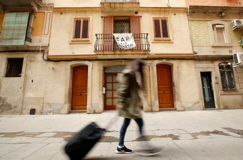 A woman pulls a suitcase through the Barceloneta neighborhood in front of a banner that reads &quot;No tourist apartments.&quot;