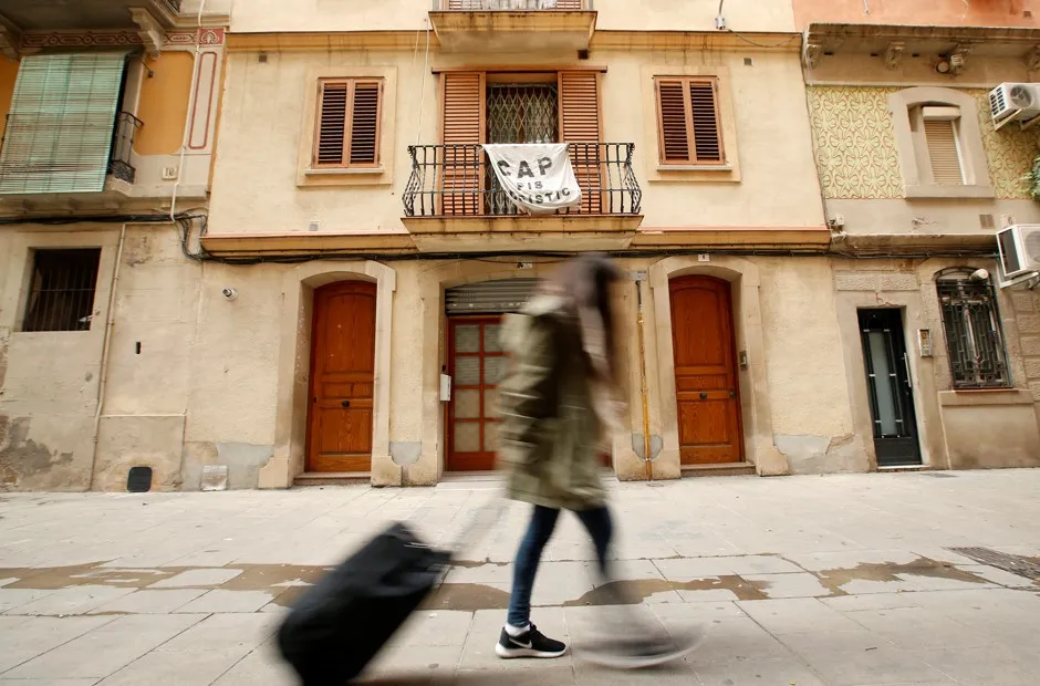 A woman pulls a suitcase through the Barceloneta neighborhood in front of a banner that reads "No tourist apartments."