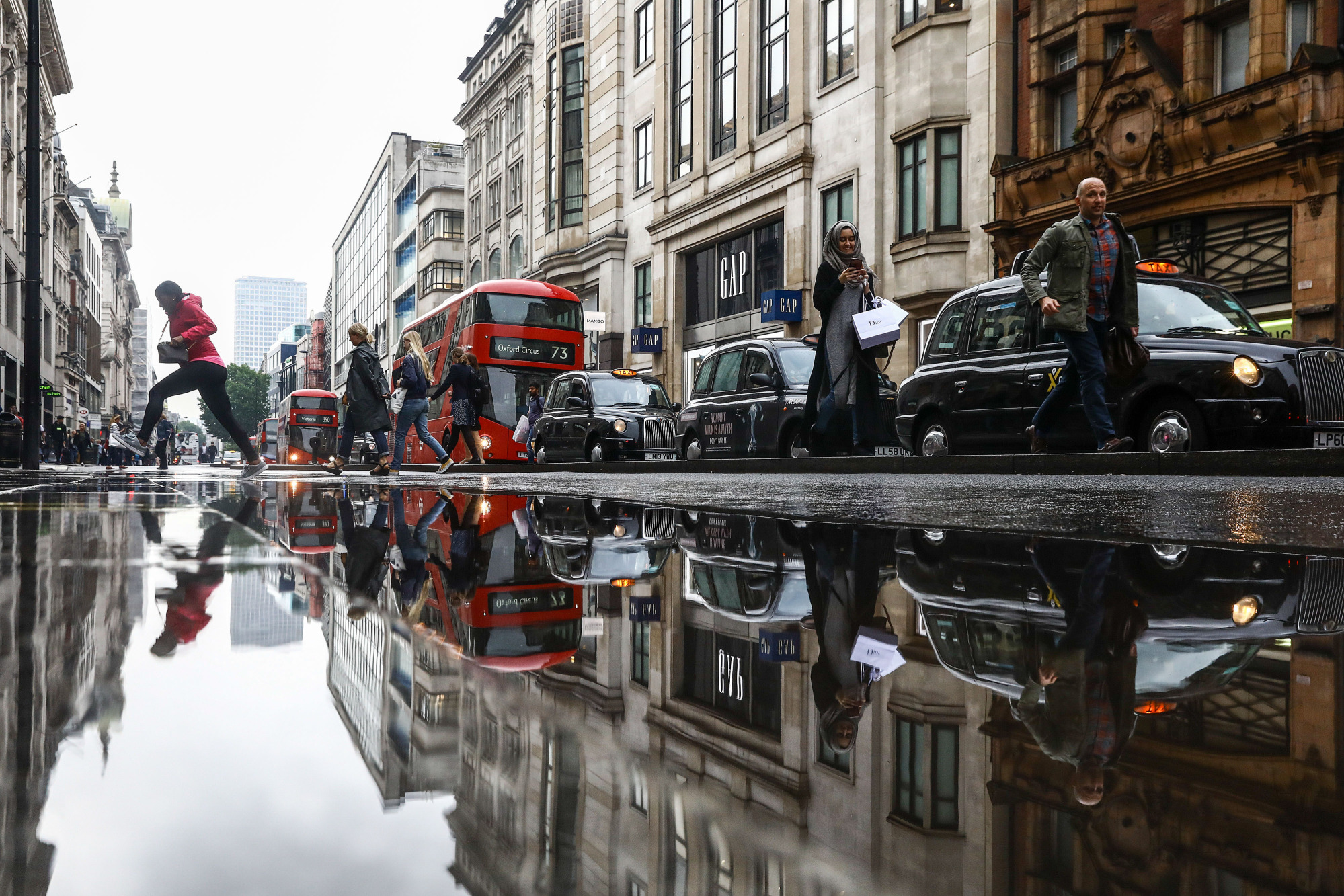 A puddle reflects pedestrians, buses, taxis in London.