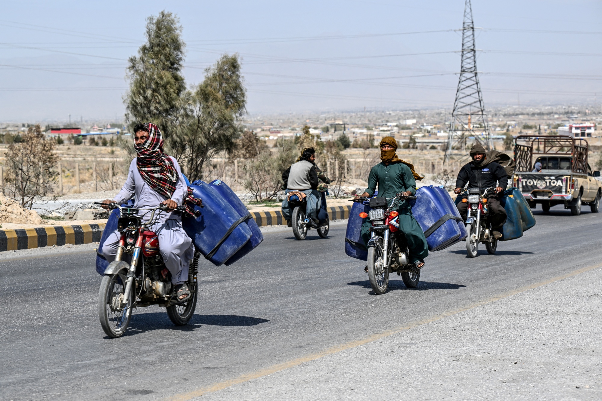 This photograph taken on March 14, 2026 shows vendors transporting jerrycans filled with smuggled Iranian petrol on their motorcycles, on the outskirts of Quetta in Balochistan province. (Photo by Banaras KHAN / AFP via Getty Images)