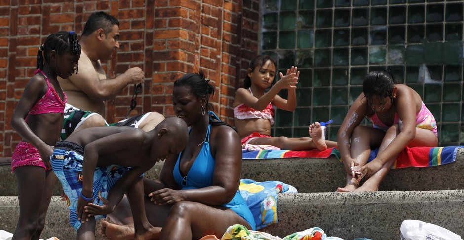 People apply sunscreen while sitting on the steps next to the Astoria Park Pool in New York.
