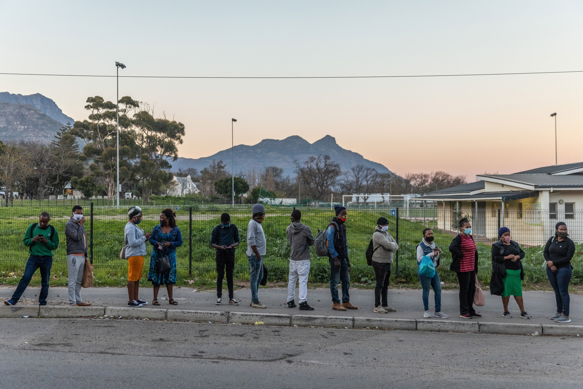 Local residents wearing protective face masks wait at a bus stop in the Imizamo Yethu township area of Hout Bay, in Cape Town.