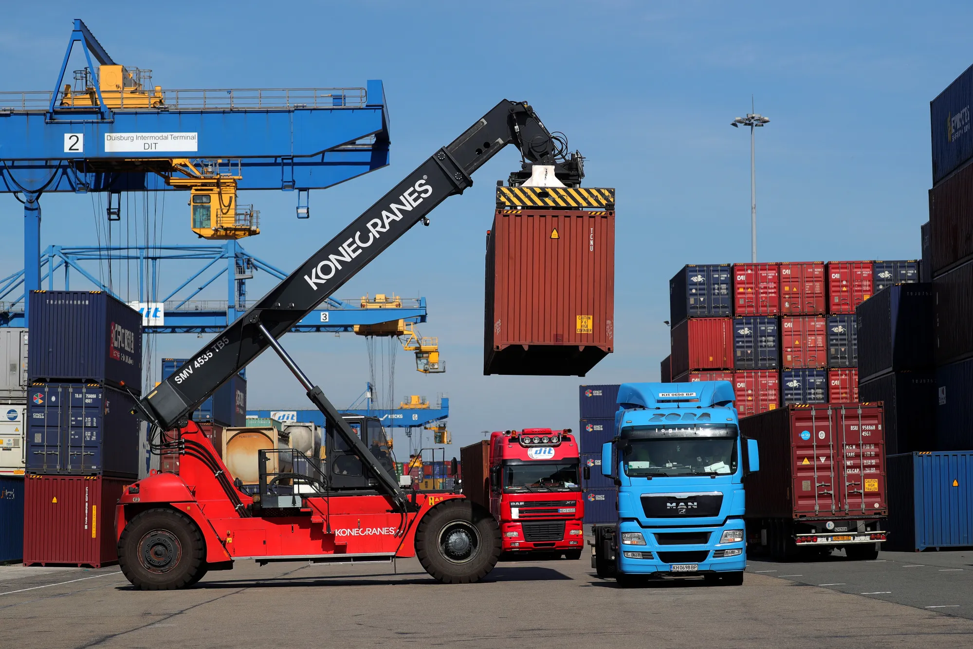 A reach stacker lowers a shipping container onto a cargo truck at Duisport shipping port.