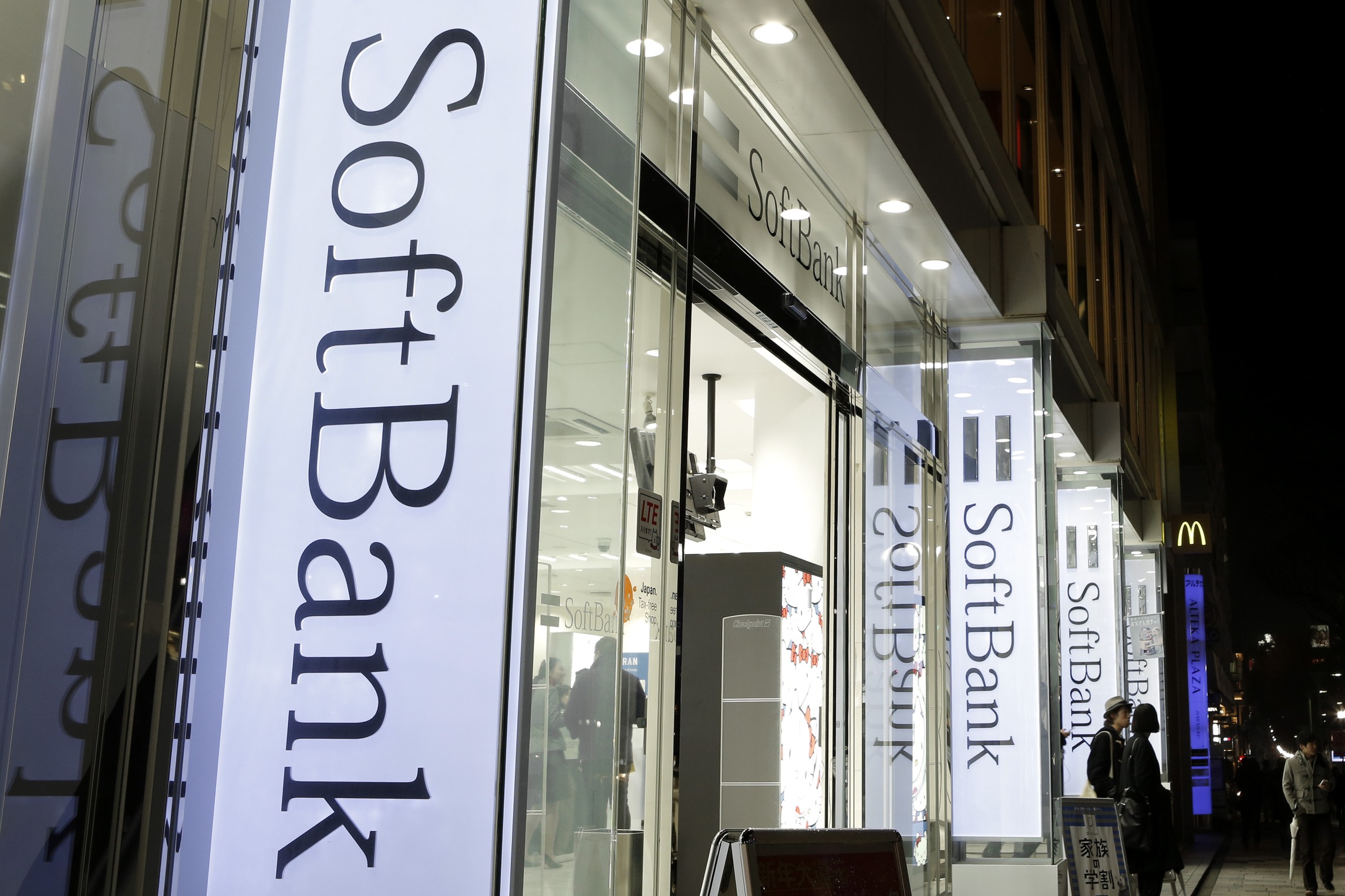 Customers exit a SoftBank Corp. store at night in Tokyo, Japan, on Sunday, Feb. 8, 2015. SoftBank, the Japanese wireless carrier led by billionaire Masayoshi Son, is scheduled to report third-quarter earnings on Feb. 10.