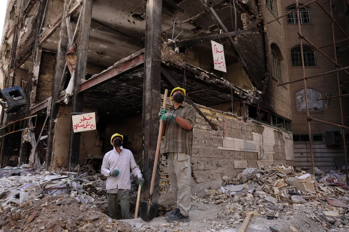 Workers look on as they stand amid the rubble of a residential building hit by airstrikes at the Shahid Broujerdi residential complex in Tehran on April 14.