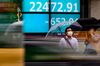 Pedestrians wearing face masks walk past an electric quotation board displaying the numbers of the Nikkei 225 Index on the Tokyo Stock Exchange in Tokyo on June 11, 2020.