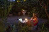 Woman cooling off in small tin tub in the garden, watching a movie on laptop
