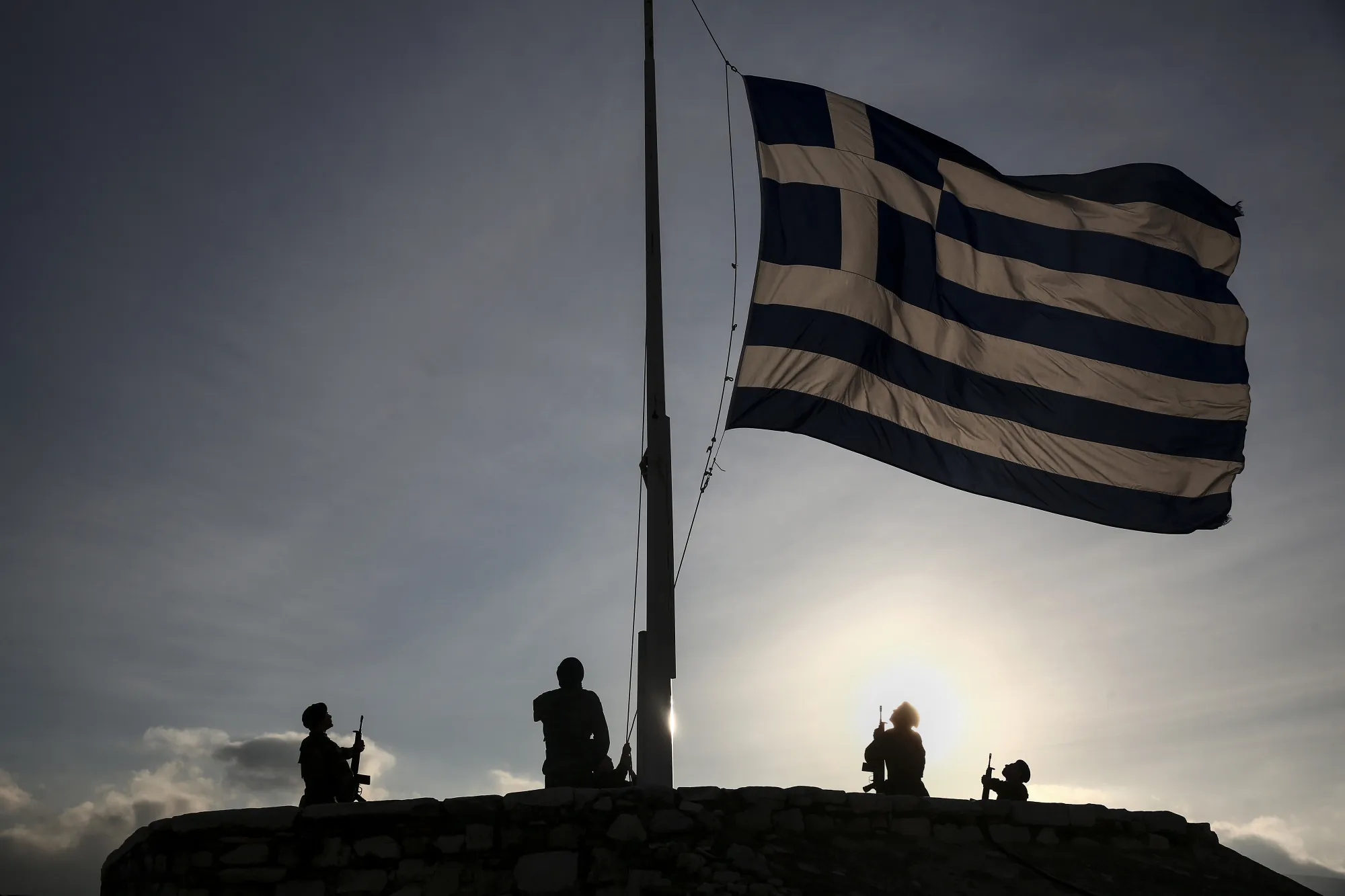 Greek army soldiers stand to attention while raising the national flag early morning on Acropolis Hill in Athens.