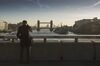 A commuter stops on London Bridge to view Tower Bridge in the distance in London, U.K., on Monday, Dec. 18, 2017. U.K. firms wanting workers face the tightest labor market in two decades. In 2011, there were almost six unemployed people for every vacancy; now there are fewer than two, the lowest ratio since records began in 2001.