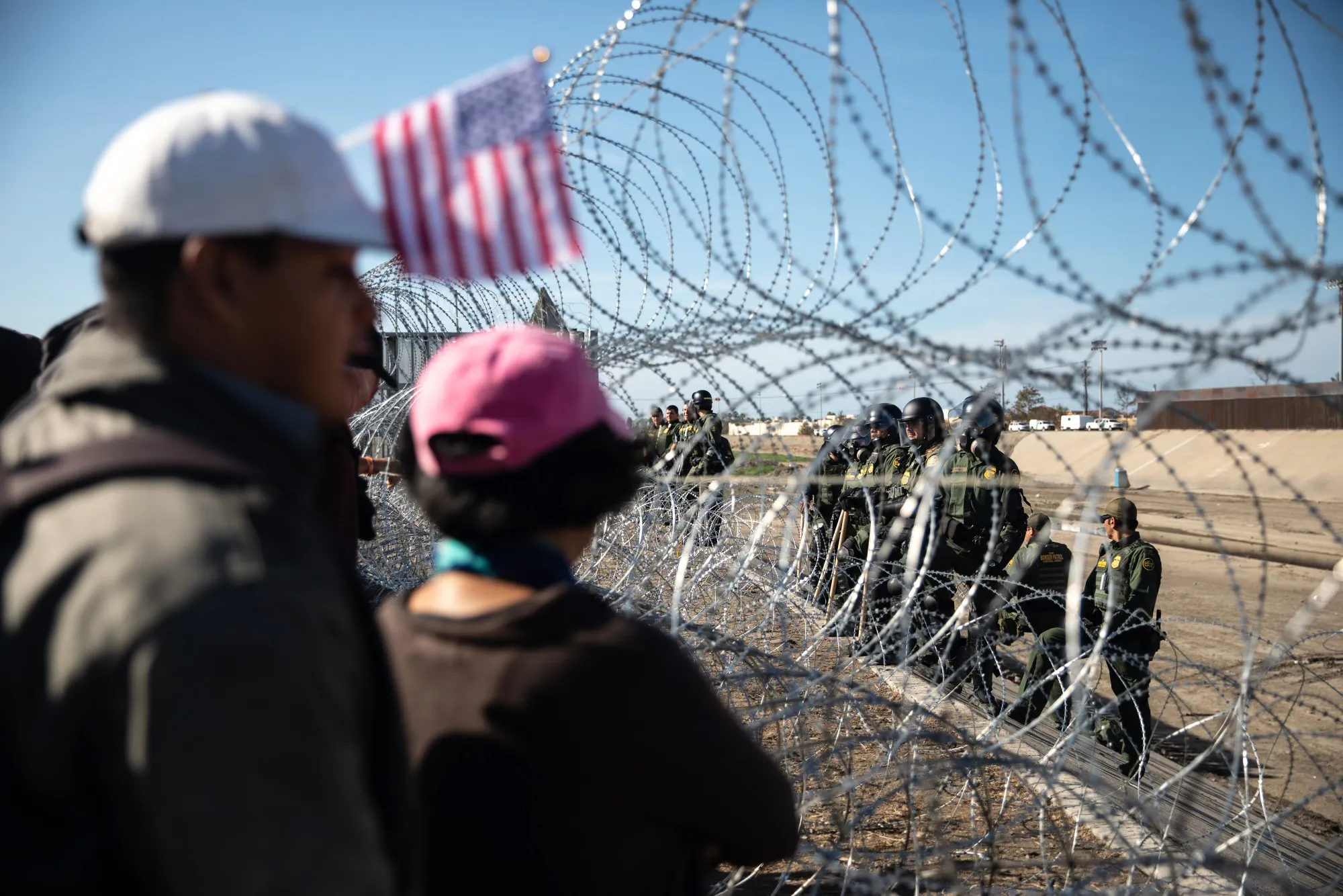 People stand in front of barbed wire across from U.S. Customs and Border Protection (CBP) officers along the US and Mexico border in Tijuana, Mexico.
