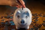 A coin is dropped into a piggy bank in this arranged photograph.