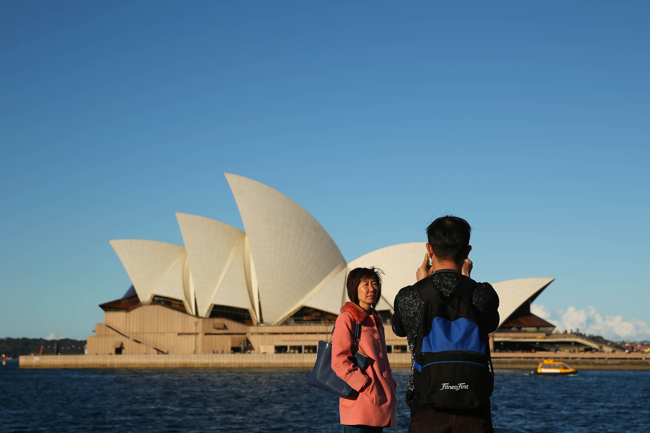 A tourist poses for photographs in front of the Sydney Opera House.
