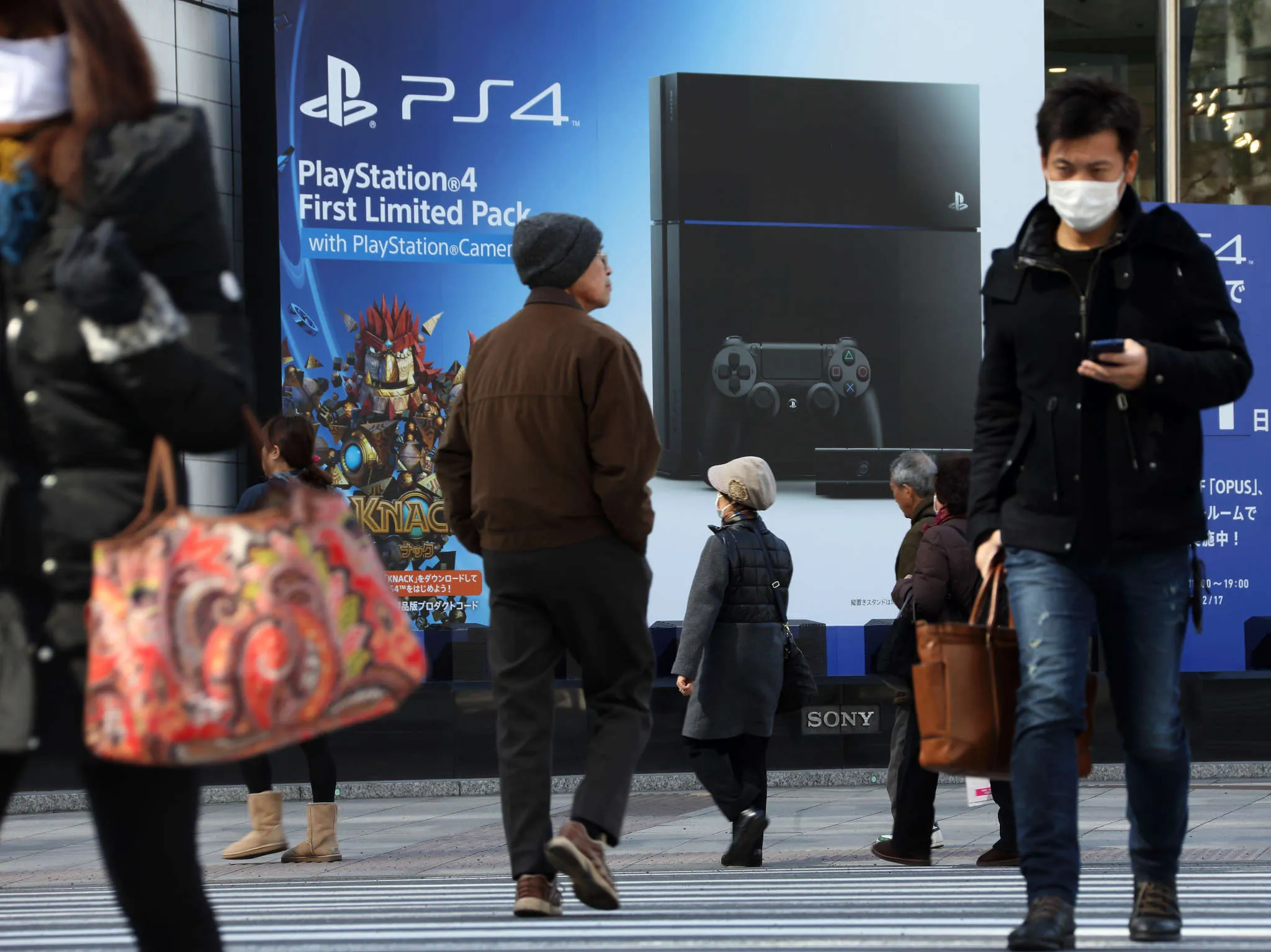 Pedestrians walk in front of an advertisement for the PlayStation 4 video game console displayed outside the Sony showroom in Tokyo.
