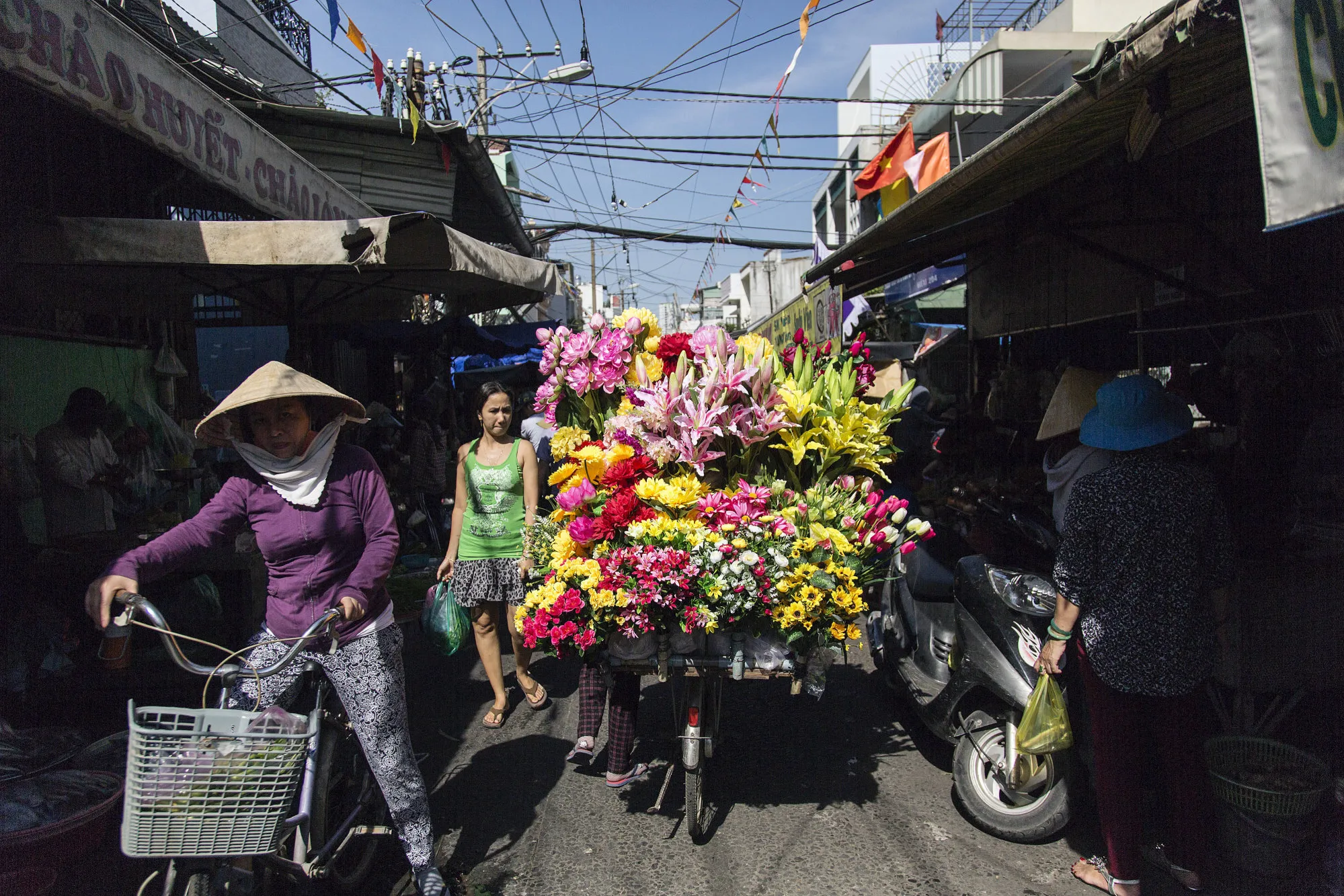 Shoppers walk past a flower vendor on a bicycle at a street market in Ho Chi Minh City.