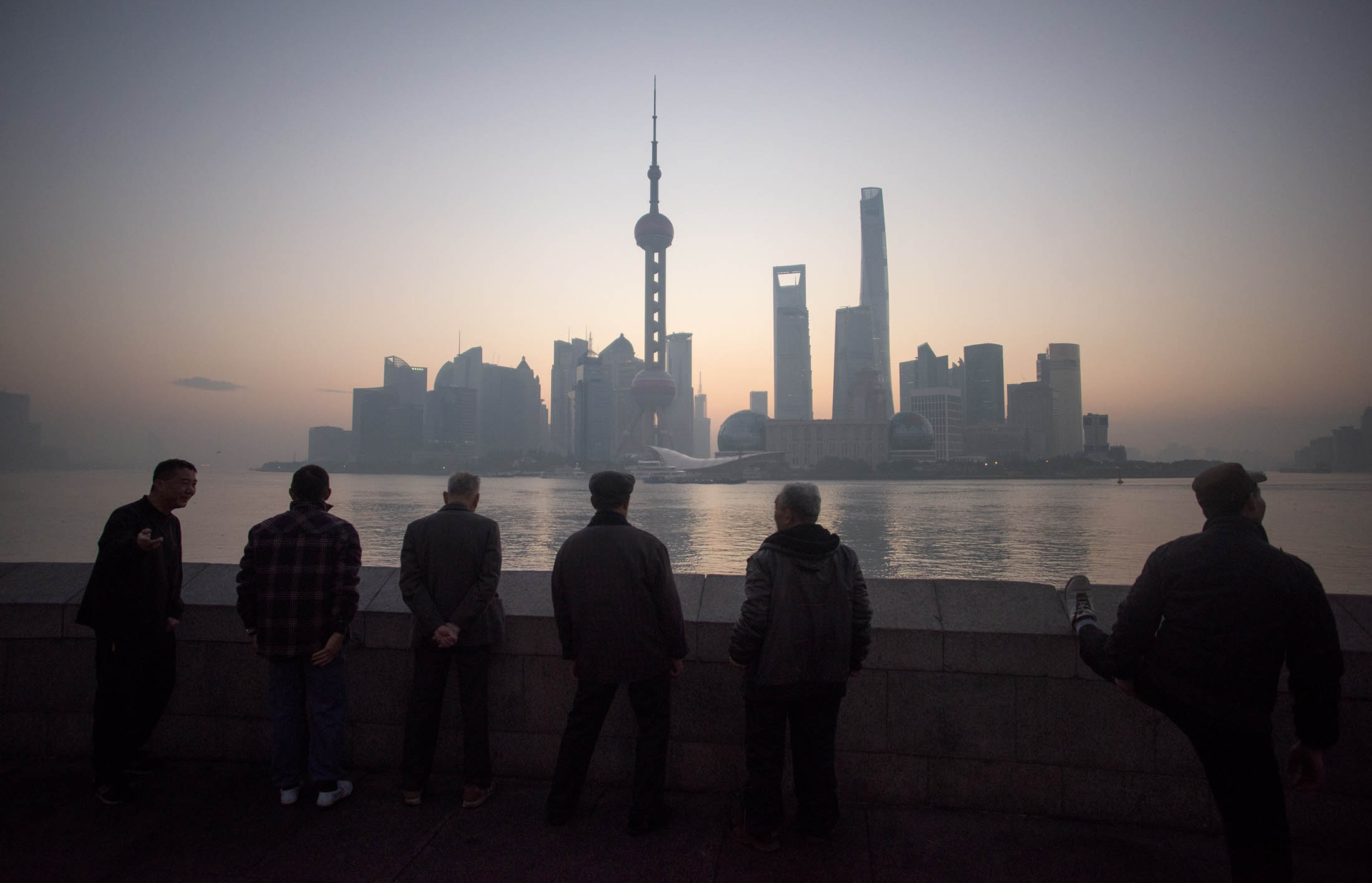 Elderly men stand together in front of the skyline of the Lujiazui Financial District in Pudong in Shanghai at dawn on December 1, 2015. AFP PHOTO / JOHANNES EISELE / AFP / JOHANNES EISELE (Photo credit should read JOHANNES EISELE/AFP/Getty Images)
