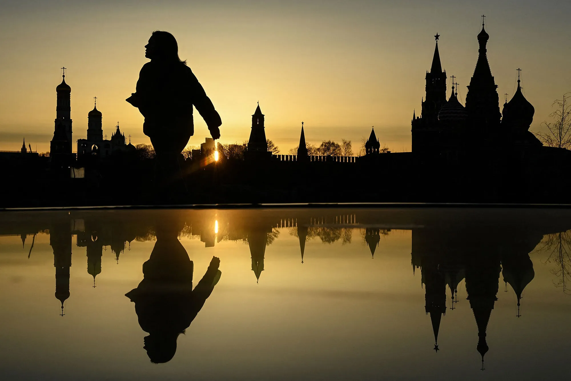 A woman walks in front of the Ivan the Great Cathedral, Kremlin’s Spasskaya tower and St Basil’s cathedral during the sunset in Moscow on March 22.