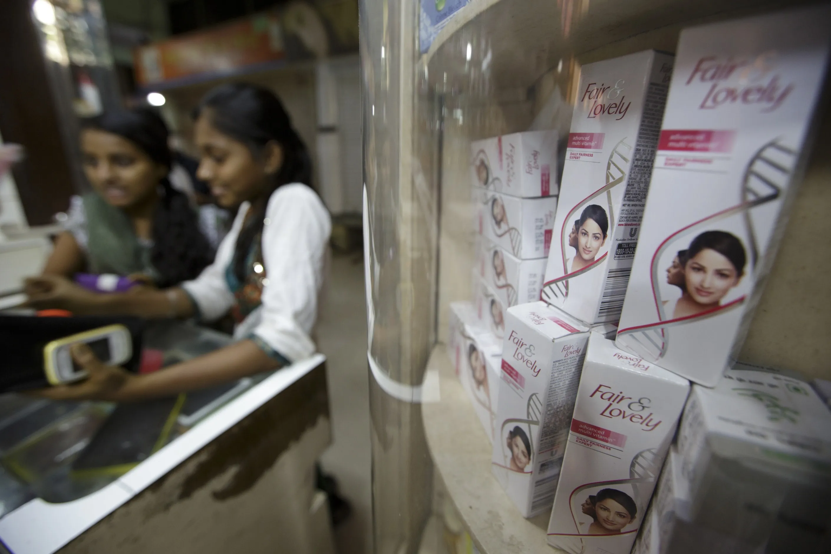 Women stand at a counter next to a shelf displaying Fair &amp; Lovely beauty products in Mumbai.