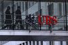 Employees pass between offices as UBS Group AG logo sits on a walkway at the UBS headquarters.