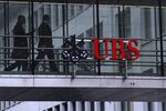 Employees pass between offices as UBS Group AG logo sits on a walkway at the UBS headquarters.