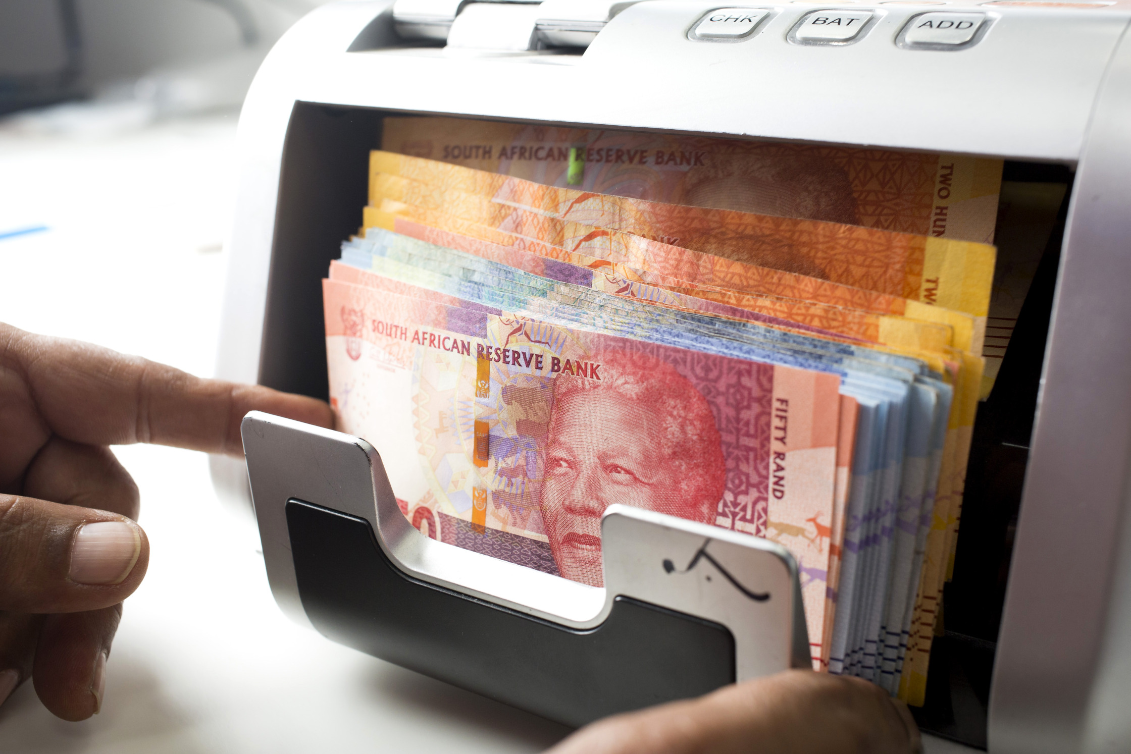 An employee uses a counting machine to count South African Rand notes .
