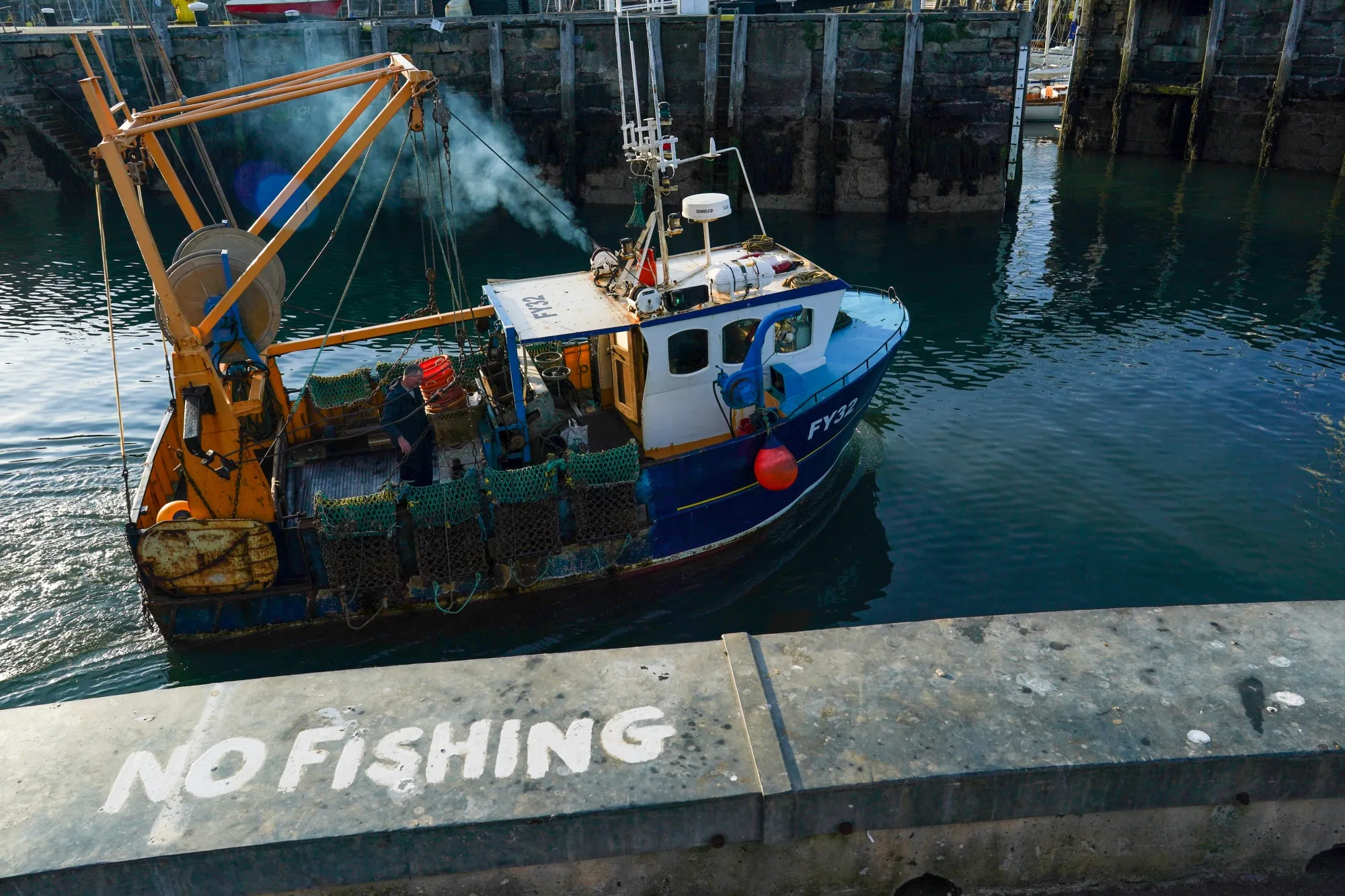 A 'No Fishing' sign sits on the quayside as a fishing boat heads out to sea from the harbour in Scarborough, U.K.