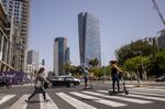 Commuters cross a street with the Azrieli Tower skyscraper in the background on April 30, 2021. An influx of tech workers has brought more e-scooters to Tel Aviv’s streets. 
