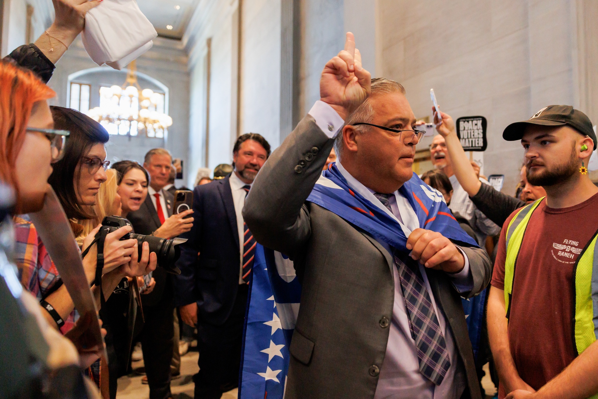 State Representative Todd Warner, a Republican from Tennessee, attempts to enter the House Floor draped in a Trump flag during a special legislative session at the Tennessee State Capitol in Nashville, Tennessee, US, on Thursday, May 7, 2026. Tennessee Gov. Bill Lee approved a new congressional map Thursday, shortly after legislators passed a redistricting plan aimed at helping Republicans win all nine of the state's US House seats. Photographer: Madison Thorn/Bloomberg 