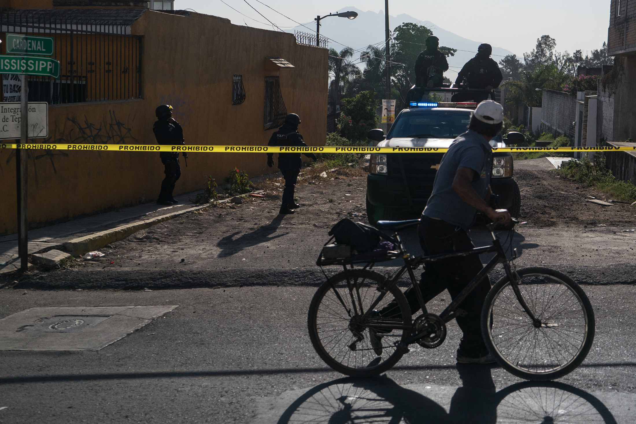 A person rides a bicycle past Nayarit police officers blocking off an area near where forces killed Juan Francisco Patrón Sánchez (known locally as H2), leader of the Beltran Leyva Cartel, the night before in the Nayarit capital of Tepic, Mexico, on Feb. 10, 2017.
