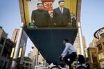 People bicycle past a giant TV screen broadcasting the meeting of North Korean leader Kim Jong Un and Chinese President Xi Jinping .