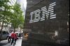 Pedestrians walk past an International Business Machines Corp. (IBM) logo.