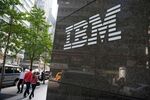 Pedestrians walk past an International Business Machines Corp. (IBM) logo.
