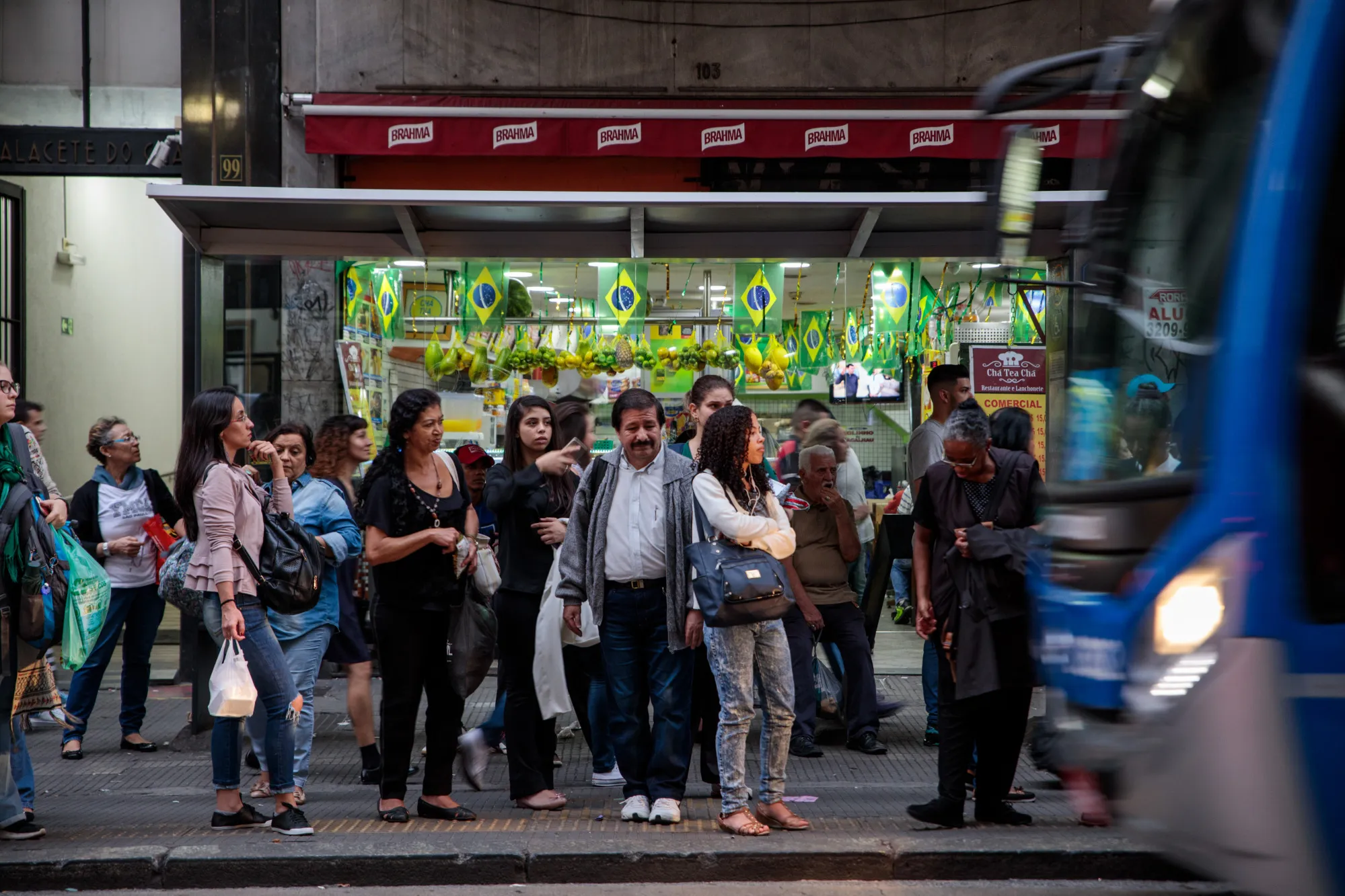 People wait at a bus stop as Brazilian flags hang in a shop&nbsp;in downtown Sao Paulo, Brazil.
