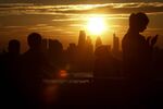 Onlookers watch the evening sun set on the horizon beyond skyscrapers in the City of London, U.K.