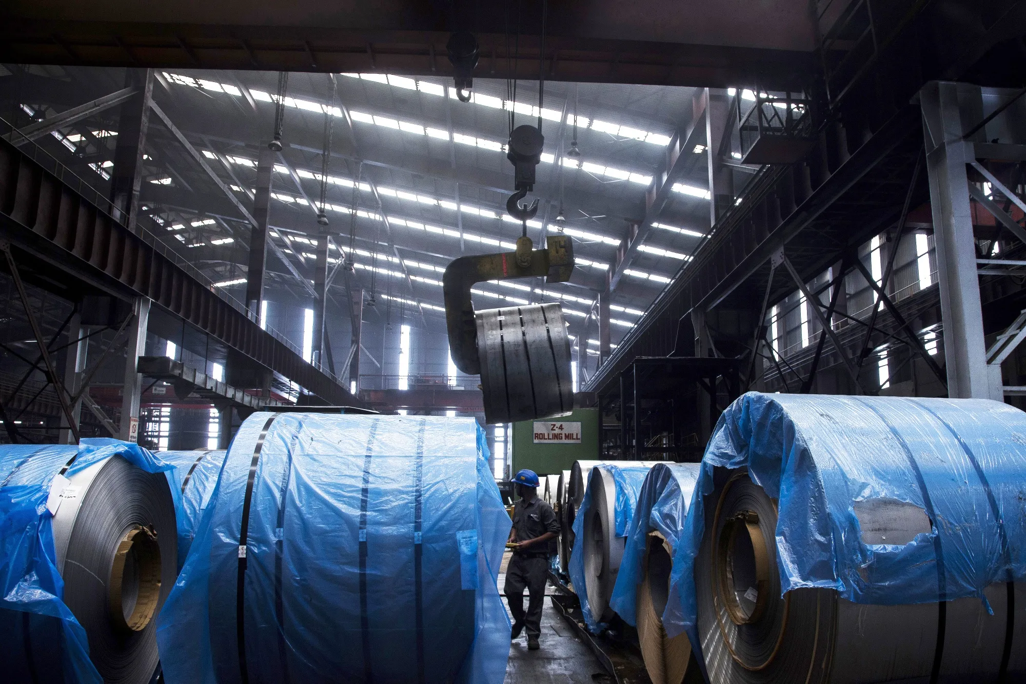 An employee walks past packaged coils of rolled steel at a Jindal Stainless factory in Hisar, India.