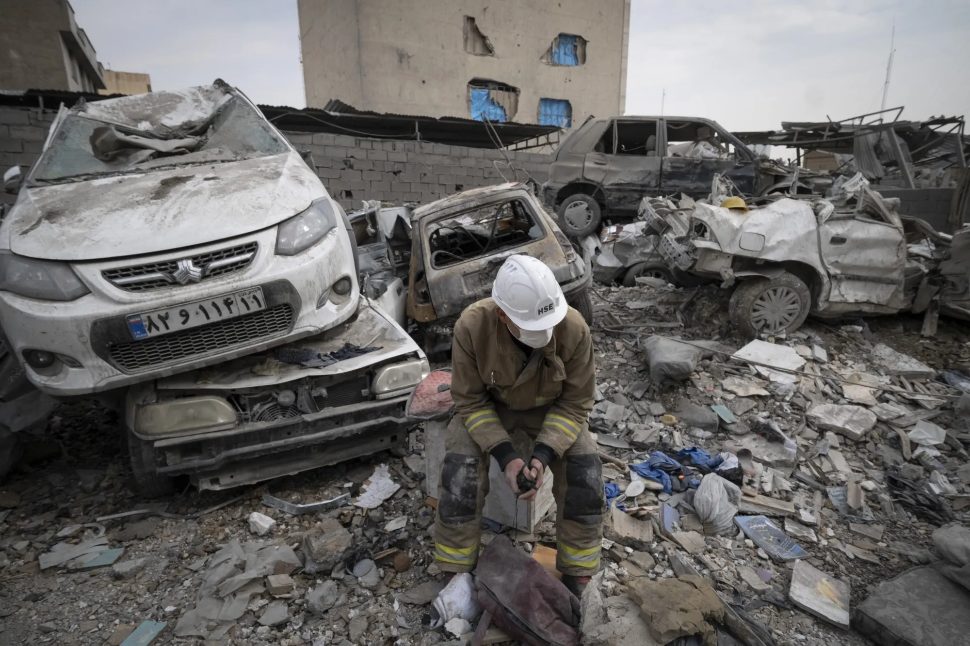 An Iranian firefighter sits in front of destroyed vehicles and the ruins of a building following strikes in Tehran on March 12.