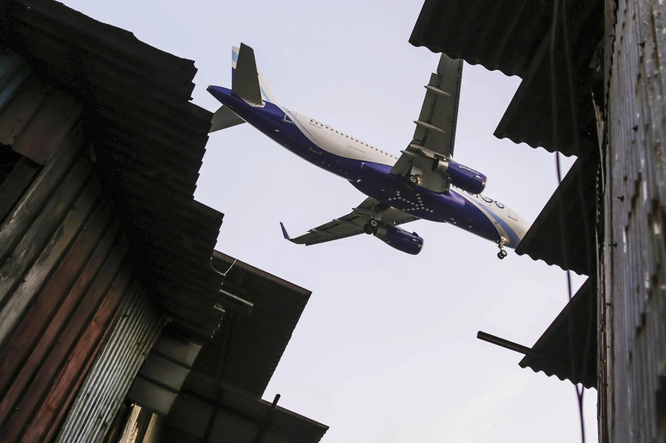 An Airbus SAS A320 aircraft operated by IndiGo flies over slum housing as it approaches to Chhatrapati Shivaji International Airport in Mumbai, India, on Saturday, June 27, 2015. IndiGo, owned by Interglobe Enterprises Ltd., is India's biggest airline by market share according to the Indian Aviation Ministry.

