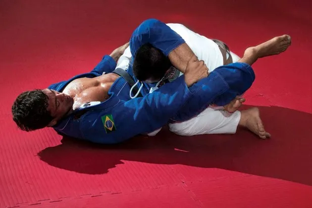 A hacker (in white and in an uncomfortable position) spars with a Brazilian jiujitsu black belt on the eve of the Infiltrate conference