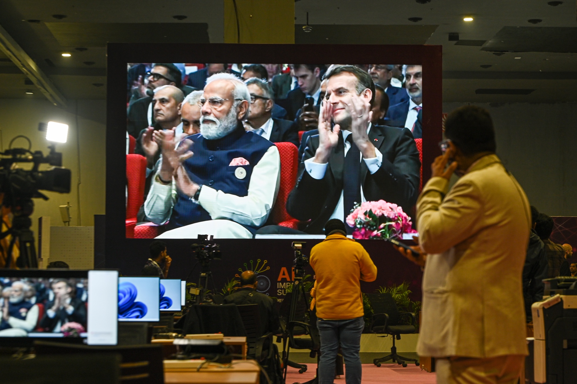 A live telecast displayed inside the media room of India's Prime Minister Narendra Modi and France's President Emmanuel Macron in the audience at the AI Impact Summit in New Delhi, India, on Thursday, Feb. 19, 2026. India kicked off one of the world's largest artificial intelligence summits this week as Prime Minister Narendra Modi seeks to make the country an AI hub amid intense competition to develop frontier models. Photographer: Prakash Singh/Bloomberg