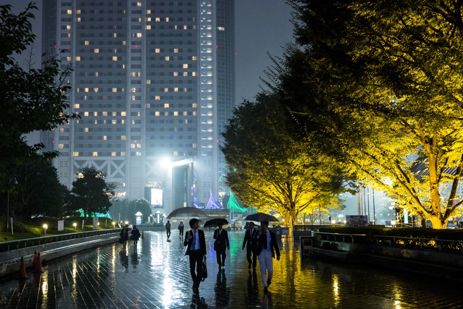 Pedestrians walk past illuminated trees on a rainy night in Tokyo. 