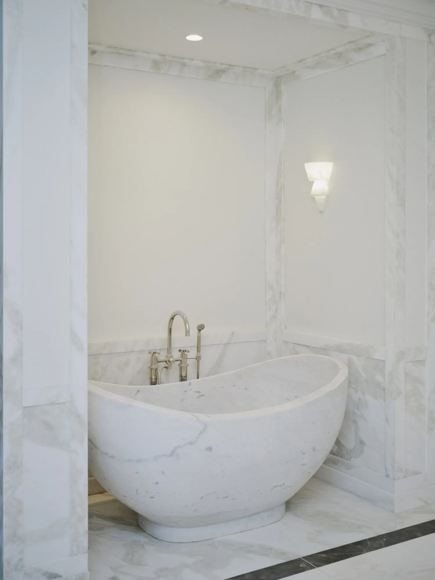 A black and white marble sink and colorful wallpaper. A white marble bath tub.