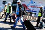 Workers wearing hard hats and hi-vis jackets pull luggage outside the venue for the Mobile World Congress in Barcelona, Spain, on Saturday, Feb. 20, 2016. Mobile World Congress, an annual phone-industry event organized by GSMA Ltd., runs from Feb 22 to Feb 25.
