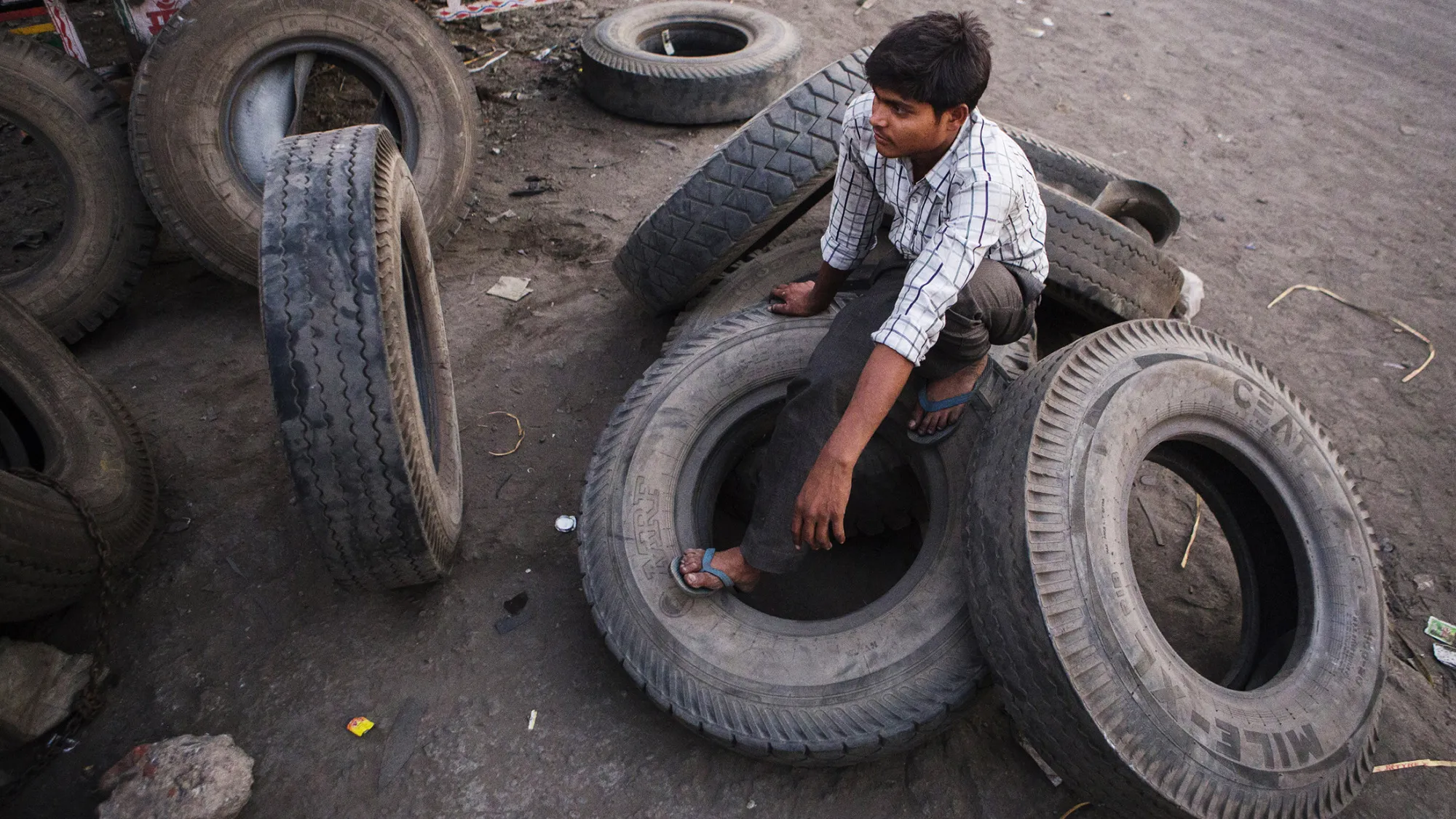 A worker sits on tires at a vehicle maintenance workshop near the Delhi city boundary in Faridabad, Haryana, India, on Friday, April 8, 2106. The odd-even car rationing plan is scheduled to return on April 15 as Delhi Supreme Court is also set to hold a hearing regarding the large vehicle diesel ban. Both measures are aimed at curbing emissions in the world's most polluted city, according to a 2014 World Health Organization database.
